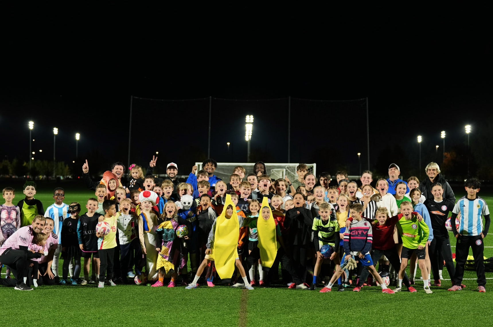 Group of children and adults on a soccer field at night